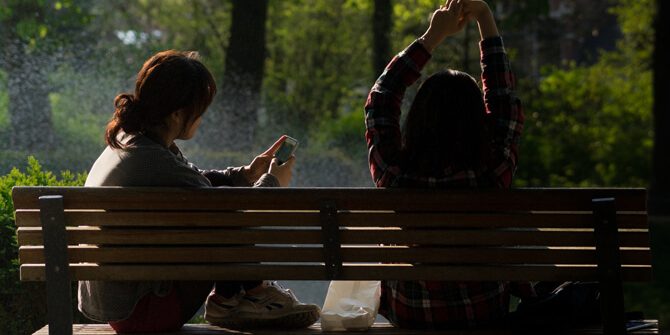 Freundinnen sitzen auf der Bank, eine schaut auf ihr Handy