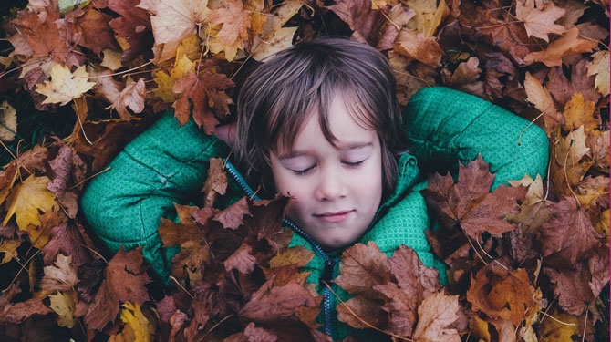 Junge liegt ohne Smartphone mit geschlossenen Augen im Laub